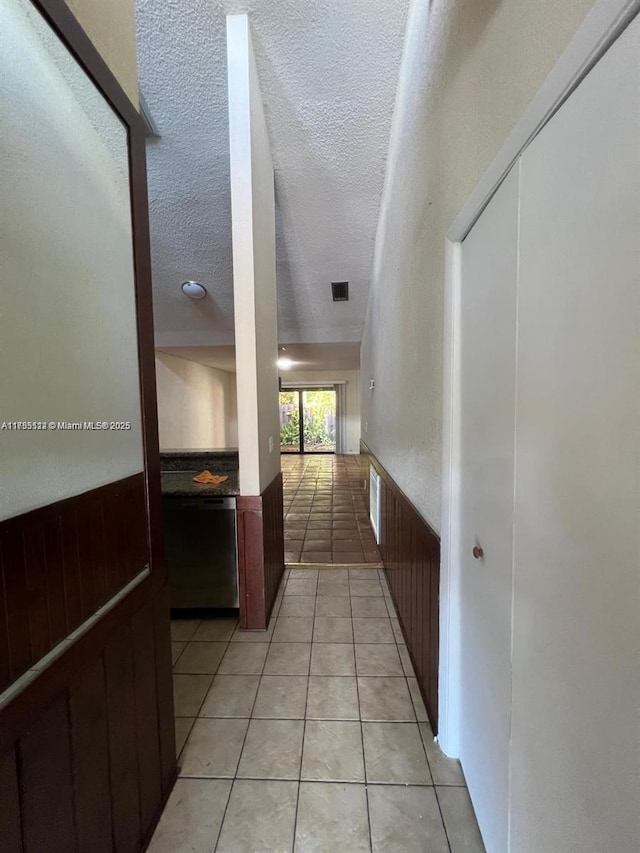 corridor with a wainscoted wall, light tile patterned floors, visible vents, and a textured ceiling