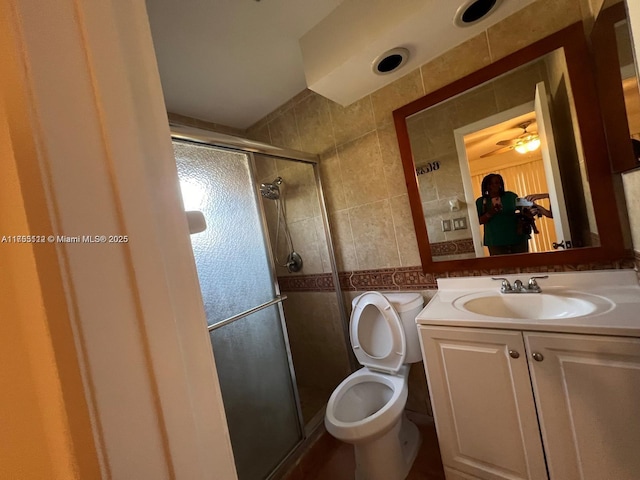 full bath with a stall shower, toilet, tile walls, and vanity