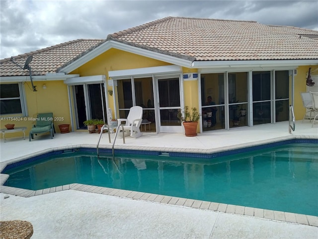 back of house with stucco siding, a tiled roof, an outdoor pool, and a patio