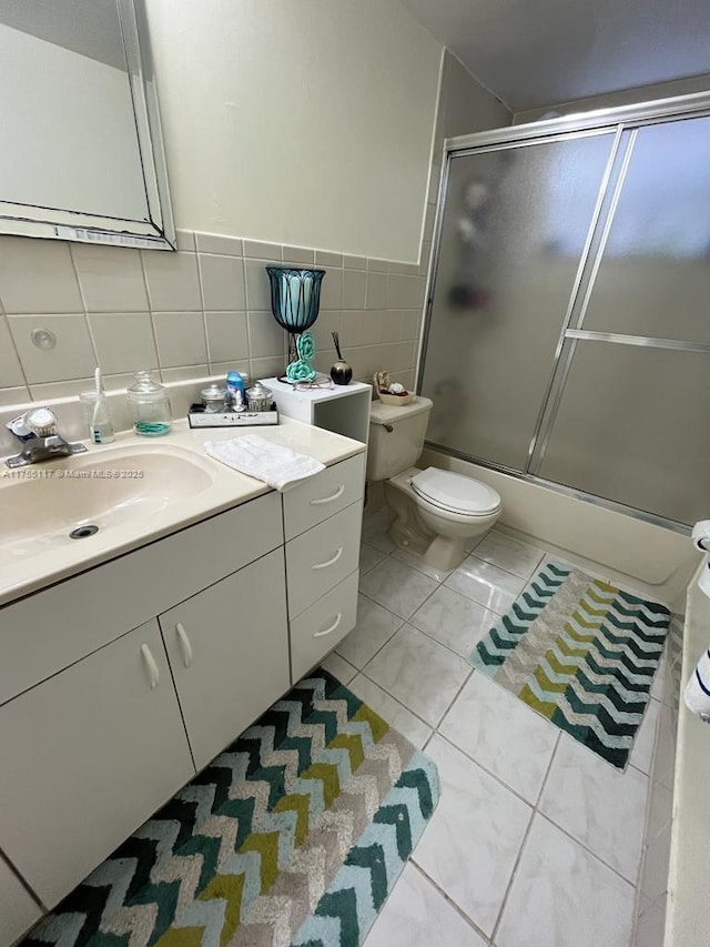 bathroom featuring tile patterned flooring, toilet, vanity, tile walls, and combined bath / shower with glass door