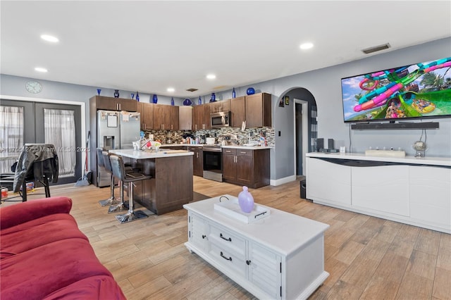 living area featuring arched walkways, light wood finished floors, visible vents, and recessed lighting