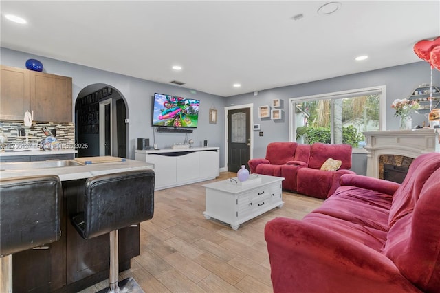 living area with arched walkways, visible vents, light wood-style flooring, a fireplace, and recessed lighting