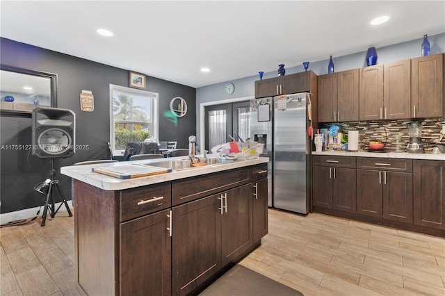 kitchen with stainless steel refrigerator with ice dispenser, light countertops, backsplash, light wood-style floors, and a kitchen island