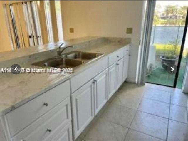 kitchen with light tile patterned flooring, a sink, light stone countertops, and white cabinets