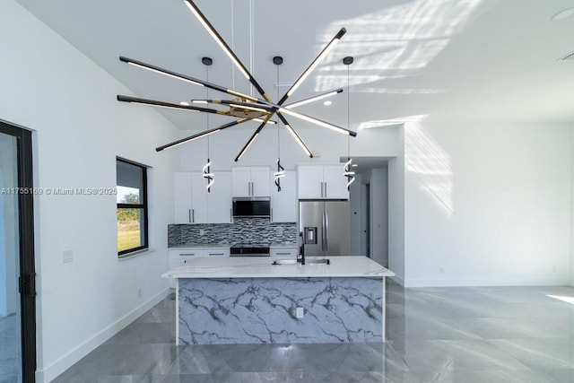 kitchen with decorative light fixtures, stainless steel appliances, decorative backsplash, white cabinets, and an island with sink