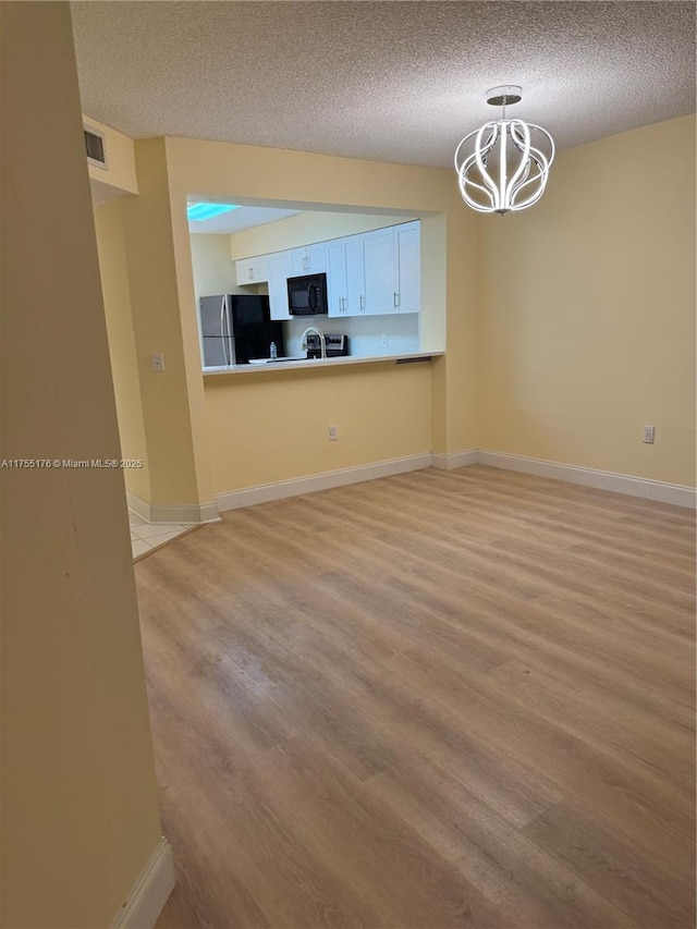 unfurnished living room with light wood-style floors, baseboards, a textured ceiling, and an inviting chandelier