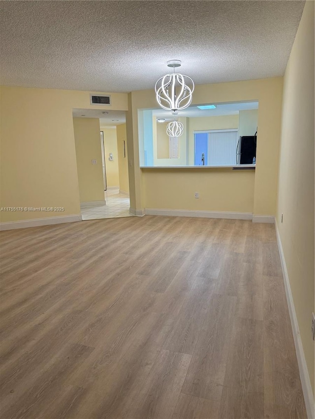 unfurnished room with a textured ceiling, wood finished floors, visible vents, and baseboards