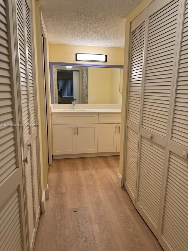 hall with a textured ceiling, light wood finished floors, and a sink