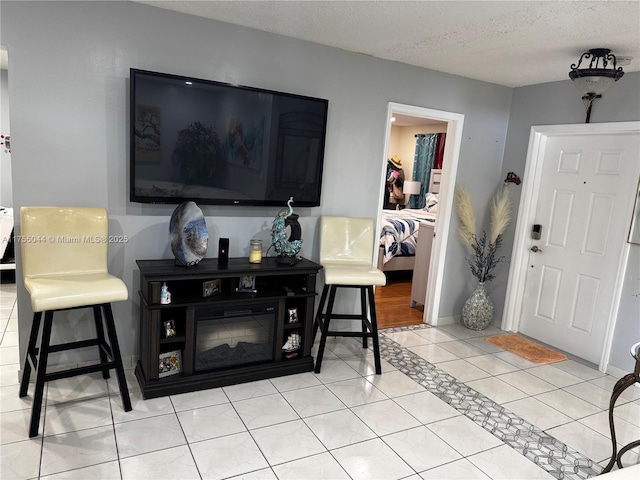 living area with light tile patterned floors, a textured ceiling, a glass covered fireplace, and baseboards