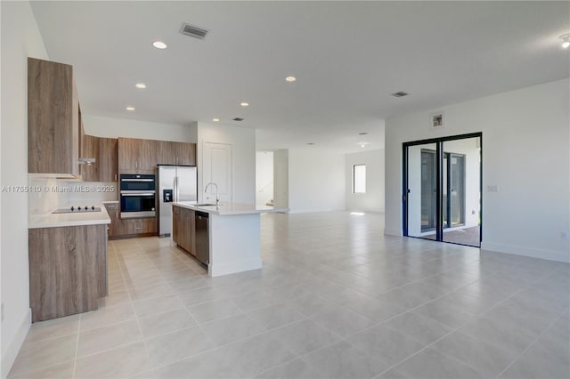 kitchen with stainless steel appliances, light countertops, brown cabinetry, open floor plan, and a sink