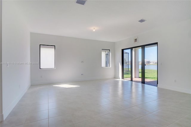 spare room with a water view, light tile patterned floors, baseboards, and visible vents