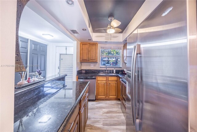 kitchen featuring visible vents, a tray ceiling, dark stone counters, a sink, and appliances with stainless steel finishes