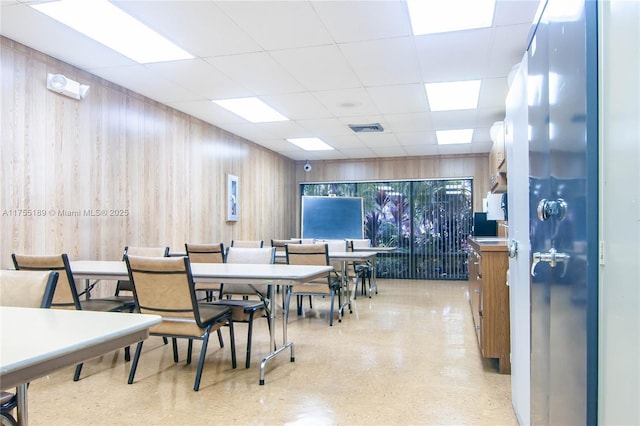 dining area with a drop ceiling, visible vents, and wood walls