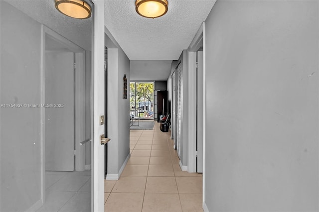 hall featuring a textured ceiling, baseboards, and light tile patterned floors