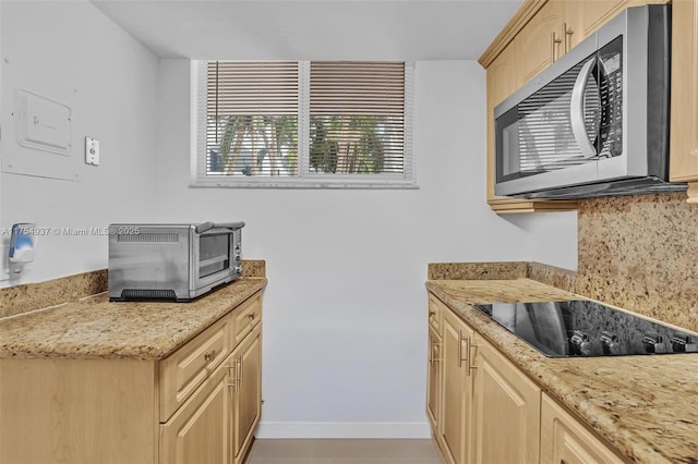 kitchen featuring tasteful backsplash, stainless steel microwave, light stone counters, black electric stovetop, and light brown cabinetry