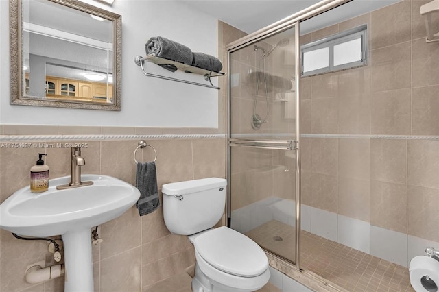 bathroom featuring toilet, a wainscoted wall, a shower stall, and tile walls