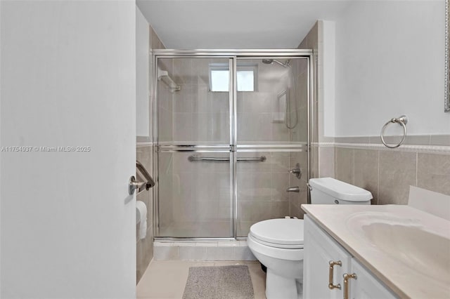 bathroom with a stall shower, wainscoting, toilet, vanity, and tile walls