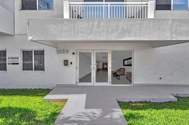 view of exterior entry featuring a balcony, a yard, a patio, and stucco siding