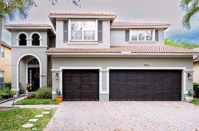 mediterranean / spanish house featuring stucco siding, an attached garage, a tile roof, and decorative driveway