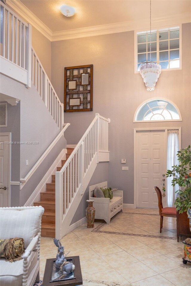 entryway featuring stairway, a healthy amount of sunlight, an inviting chandelier, and ornamental molding