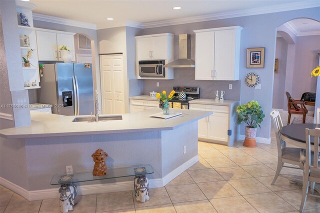 kitchen with light countertops, appliances with stainless steel finishes, arched walkways, wall chimney exhaust hood, and a sink