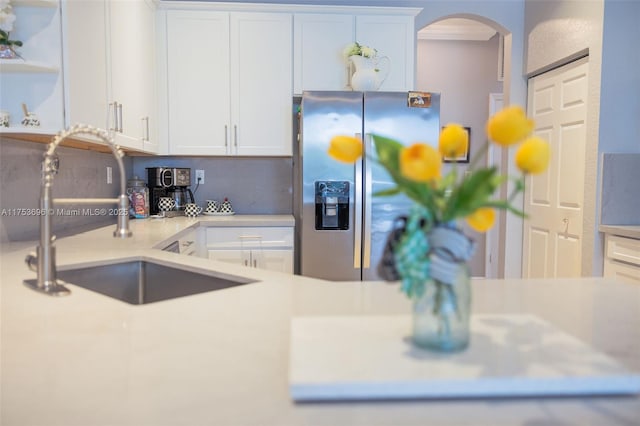 kitchen featuring stainless steel fridge with ice dispenser, light countertops, arched walkways, white cabinets, and a sink