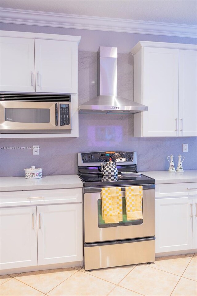 kitchen featuring light countertops, white cabinets, appliances with stainless steel finishes, crown molding, and wall chimney range hood