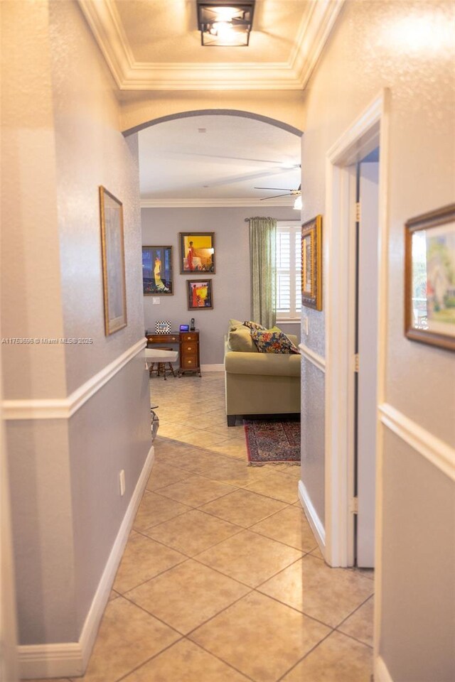 hall featuring arched walkways, light tile patterned floors, baseboards, and ornamental molding