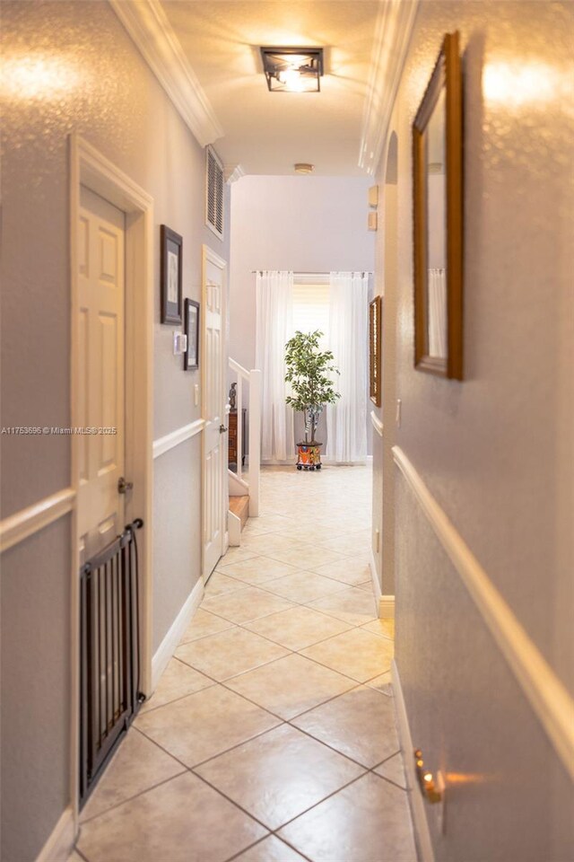 corridor featuring light tile patterned floors, visible vents, baseboards, and ornamental molding