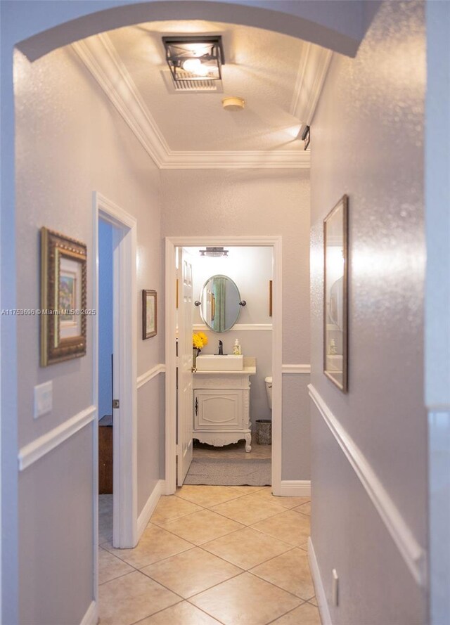 hall featuring light tile patterned floors, baseboards, arched walkways, a sink, and crown molding