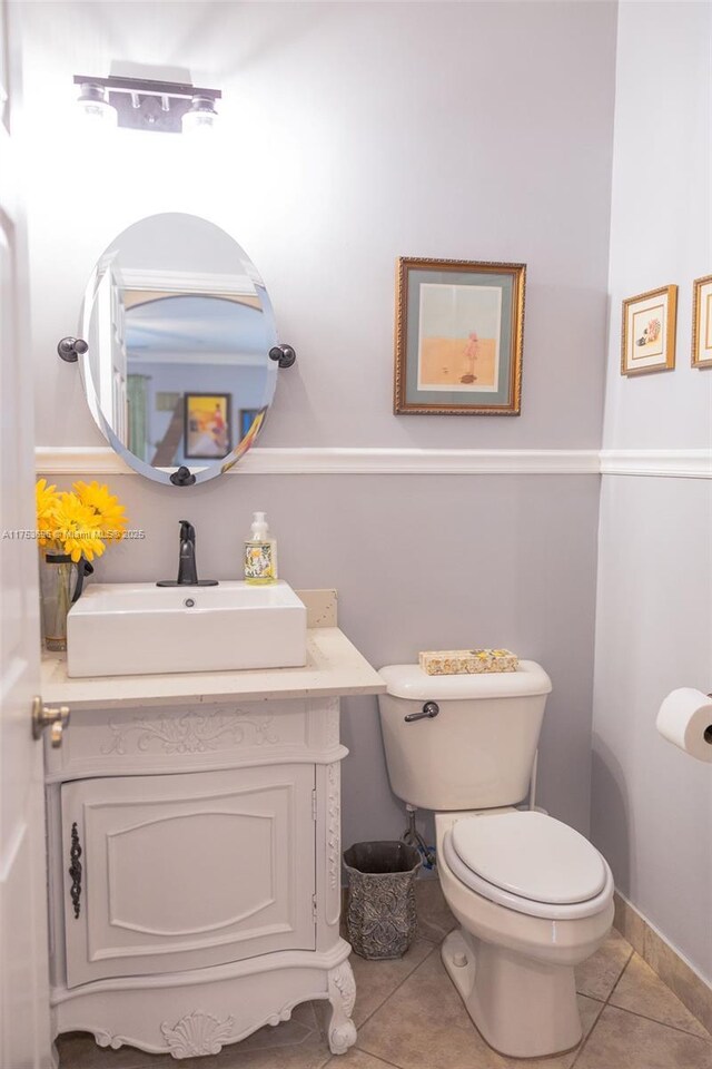 half bathroom with vanity, tile patterned floors, toilet, and baseboards