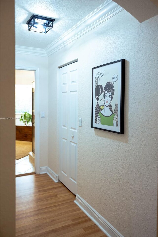 hall featuring baseboards, wood finished floors, ornamental molding, a textured wall, and a textured ceiling