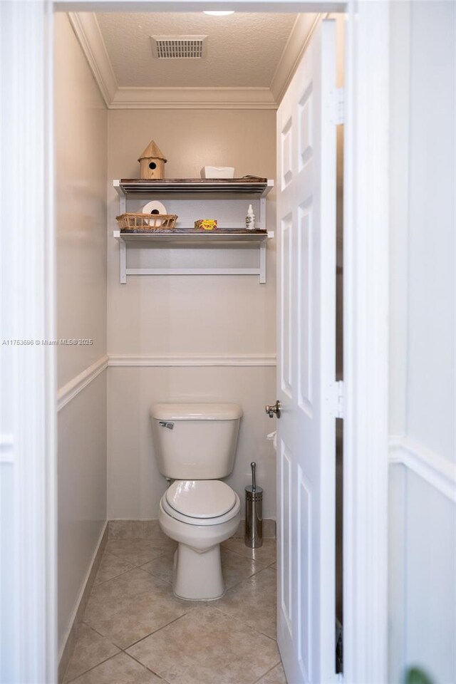 bathroom with tile patterned floors, visible vents, toilet, crown molding, and baseboards