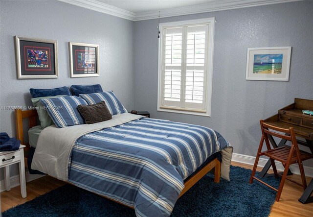 bedroom with wood finished floors, baseboards, a textured wall, and ornamental molding