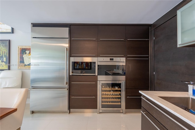 kitchen featuring dark brown cabinetry, beverage cooler, appliances with stainless steel finishes, and light tile patterned flooring