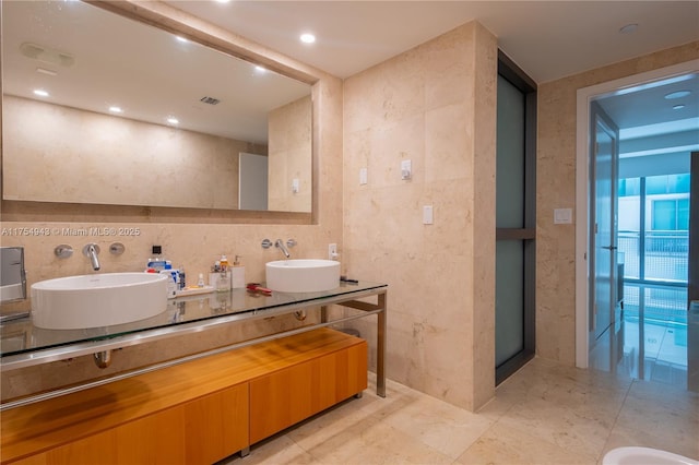 bathroom with double vanity, visible vents, tile walls, and a sink