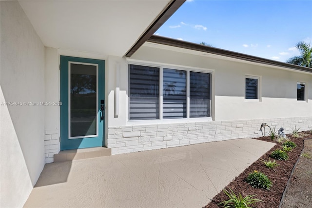 view of exterior entry featuring stone siding and stucco siding