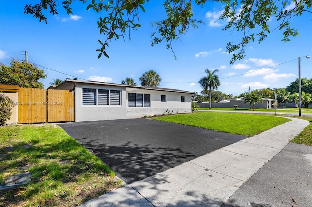 view of front of house featuring driveway, stucco siding, a gate, fence, and a front yard