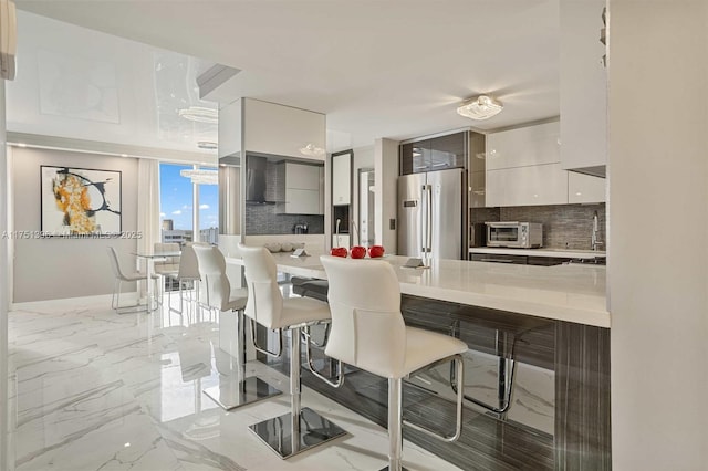 kitchen with a breakfast bar, decorative backsplash, freestanding refrigerator, modern cabinets, and a peninsula