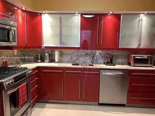 kitchen with a toaster, red cabinetry, decorative backsplash, appliances with stainless steel finishes, and a sink