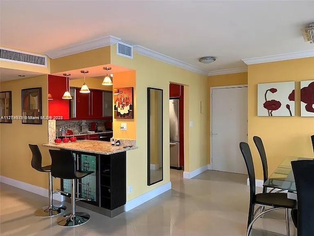 kitchen with baseboards, visible vents, ornamental molding, a breakfast bar area, and freestanding refrigerator