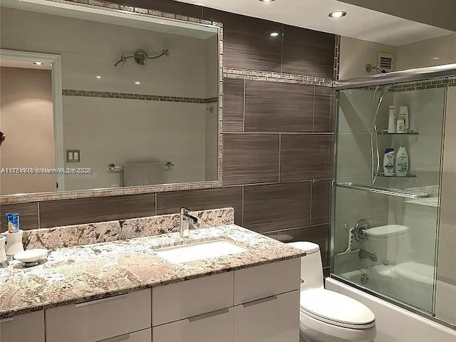 full bathroom with toilet, bath / shower combo with glass door, vanity, and tile walls