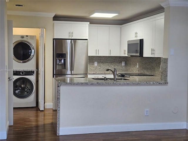 kitchen with a peninsula, light stone countertops, stainless steel appliances, stacked washing maching and dryer, and a sink