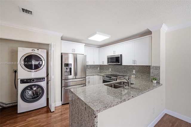 12611 SW 54th Ct Unit 12611, Miramar, FL 33027 - kitchen featuring appliances with stainless steel finishes, stacked washer / drying machine, a peninsula, light stone counters, and crown molding