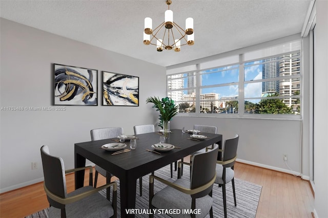 dining space with a textured ceiling, baseboards, a notable chandelier, and light wood-style floors