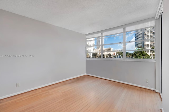 empty room featuring wood-type flooring, baseboards, a city view, and a textured ceiling