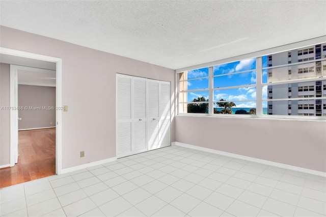 unfurnished bedroom featuring tile patterned flooring, a textured ceiling, baseboards, and a closet