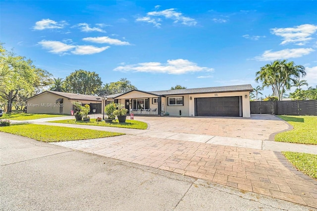 ranch-style house with an attached garage, fence, decorative driveway, a front lawn, and stucco siding