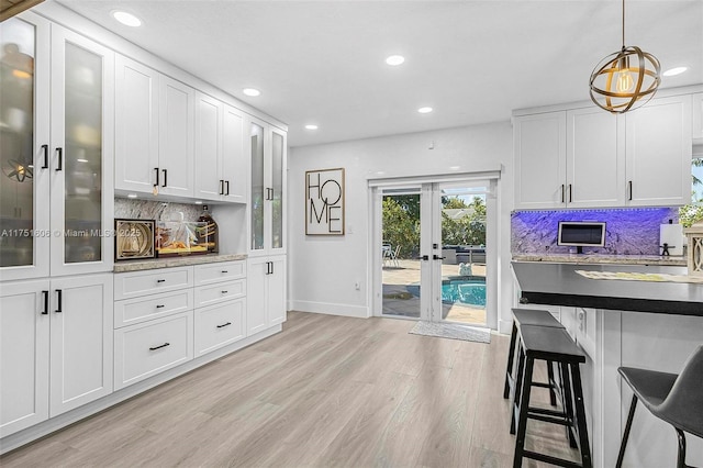 kitchen with french doors, a breakfast bar area, light wood-style flooring, backsplash, and white cabinetry