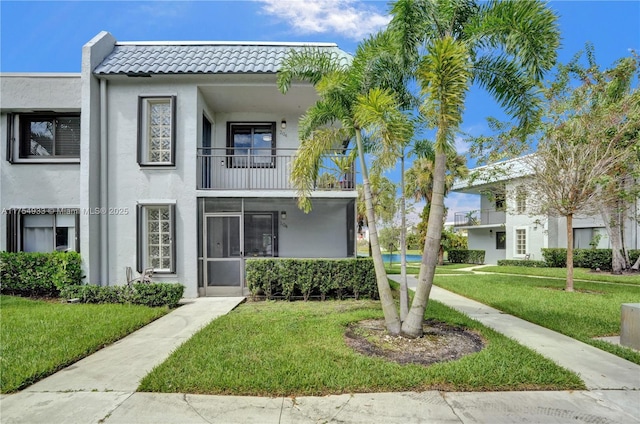 view of property featuring a balcony, a tiled roof, a front lawn, and stucco siding